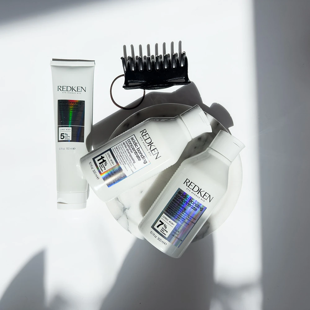 Redken hair care products and a black styling comb arranged on white background with dramatic shadows