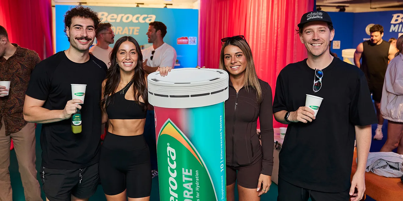 Four people pose with a large Berocca product display at a promotional event, with red curtains and branded banners in the background.