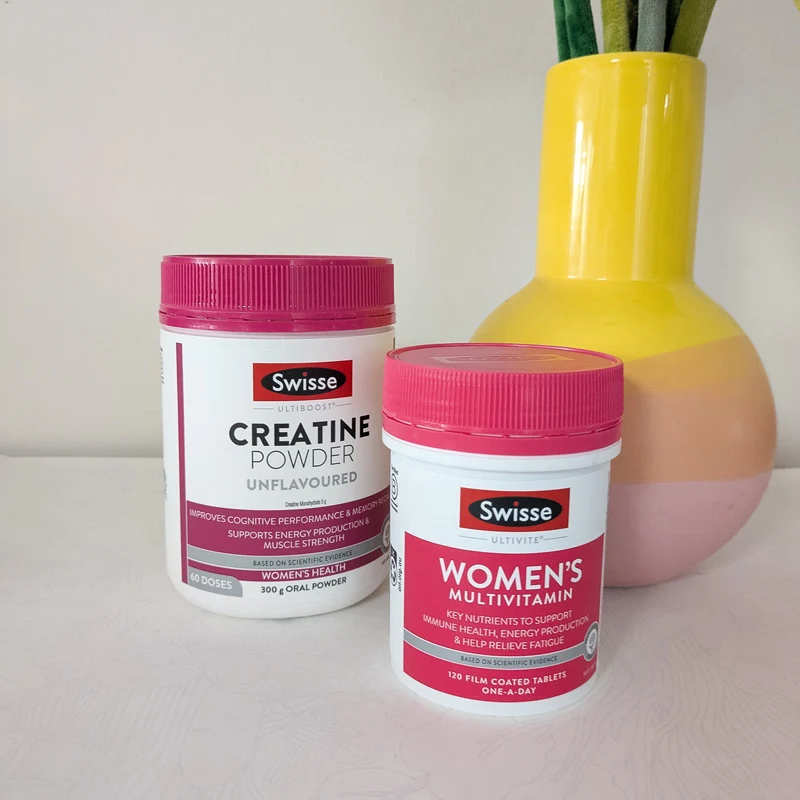 Two Swisse supplement containers: Creatine Powder and Women's Multivitamin, with pink lids, beside a yellow and pink vase.