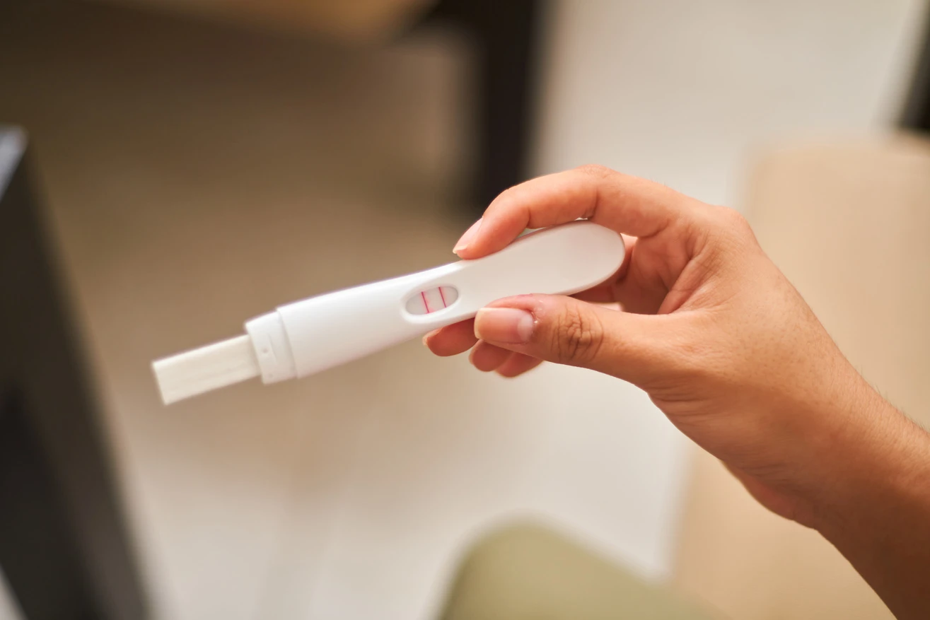 Hands holding a white pregnancy test showing two pink lines indicating a positive result