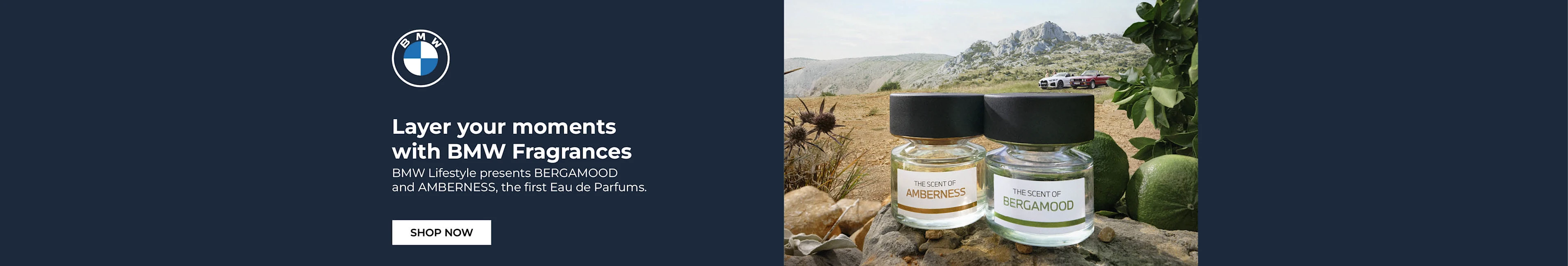 Two BMW fragrance bottles, Bergamood and Amberness, displayed on rocky terrain with luxury cars in the mountain backdrop