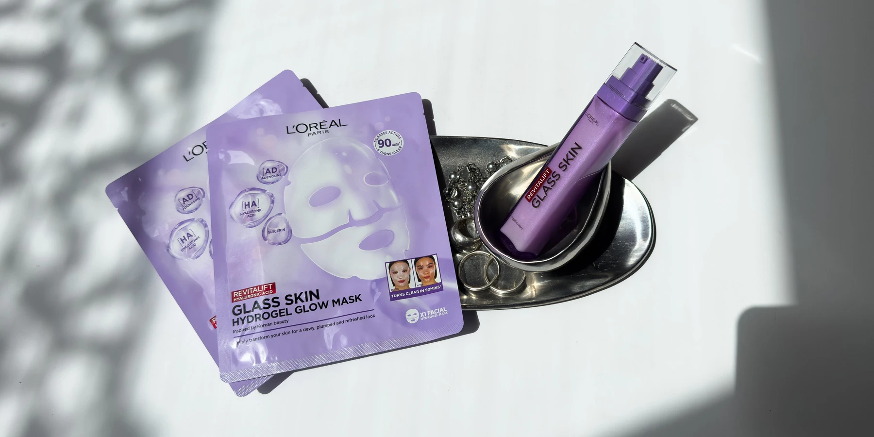 Purple L'Oreal Paris Revitalift Glass Skin Hydrogel Glow face mask packets displayed on reflective metallic surface