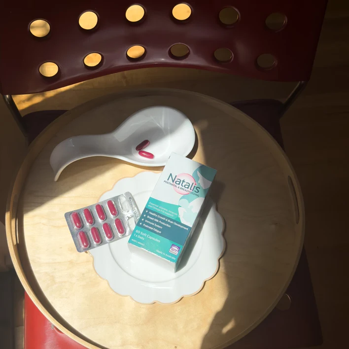 Natalis prenatal vitamin package and blister pack of red pills displayed on white scalloped plate under spotlight illumination