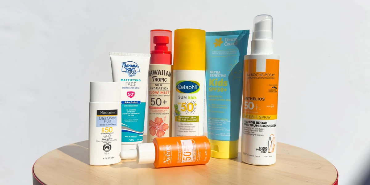 Seven sunscreen products on a wooden table, including Neutrogena, Banana Boat, Hawaiian Tropic, Cetaphil, Avene, Cancer Council, and La Roche-Posay.