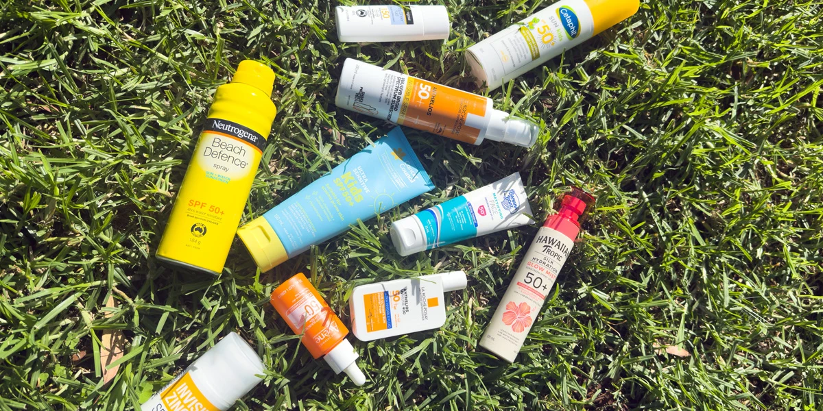 Various sunscreen products including Neutrogena and Hawaiian Tropic SPF 50+ scattered on green grass in sunlight.