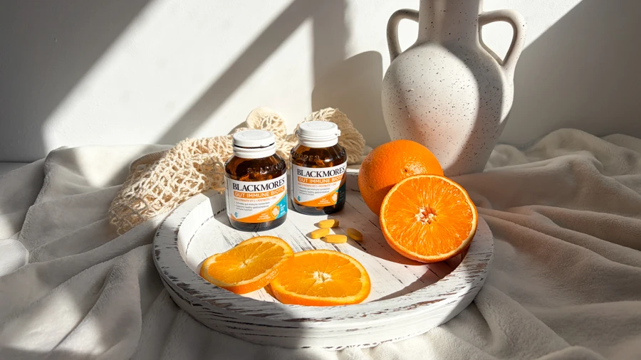 Two Blackmores Gut Immune Boost supplement bottles on a white tray with fresh orange slices, a white ceramic vase nearby.