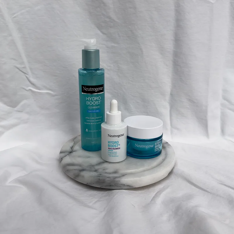 Three Neutrogena Hydro Boost skincare products displayed on a round marble surface against white fabric background.