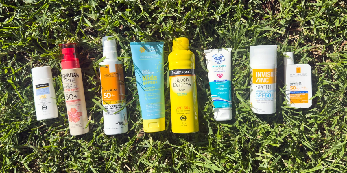Eight sunscreen products laid on green grass, including brands like Neutrogena, Hawaiian Tropic, La Roche-Posay, and Banana Boat.