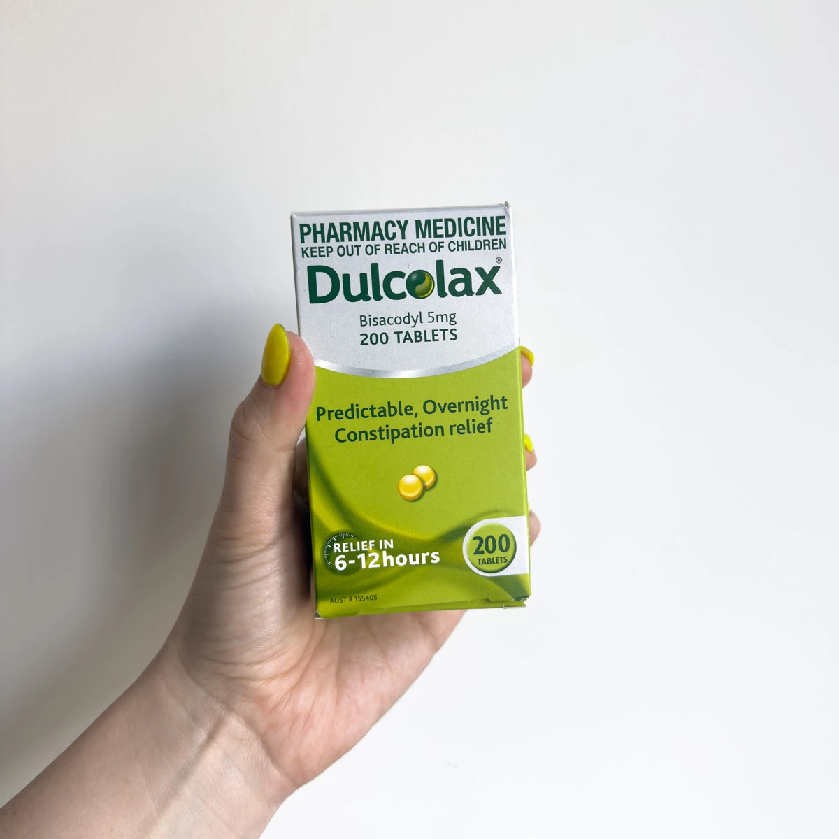 A hand with yellow nails holding a green and white Dulcolax Bisacodyl 5mg 200 tablets box for constipation relief.