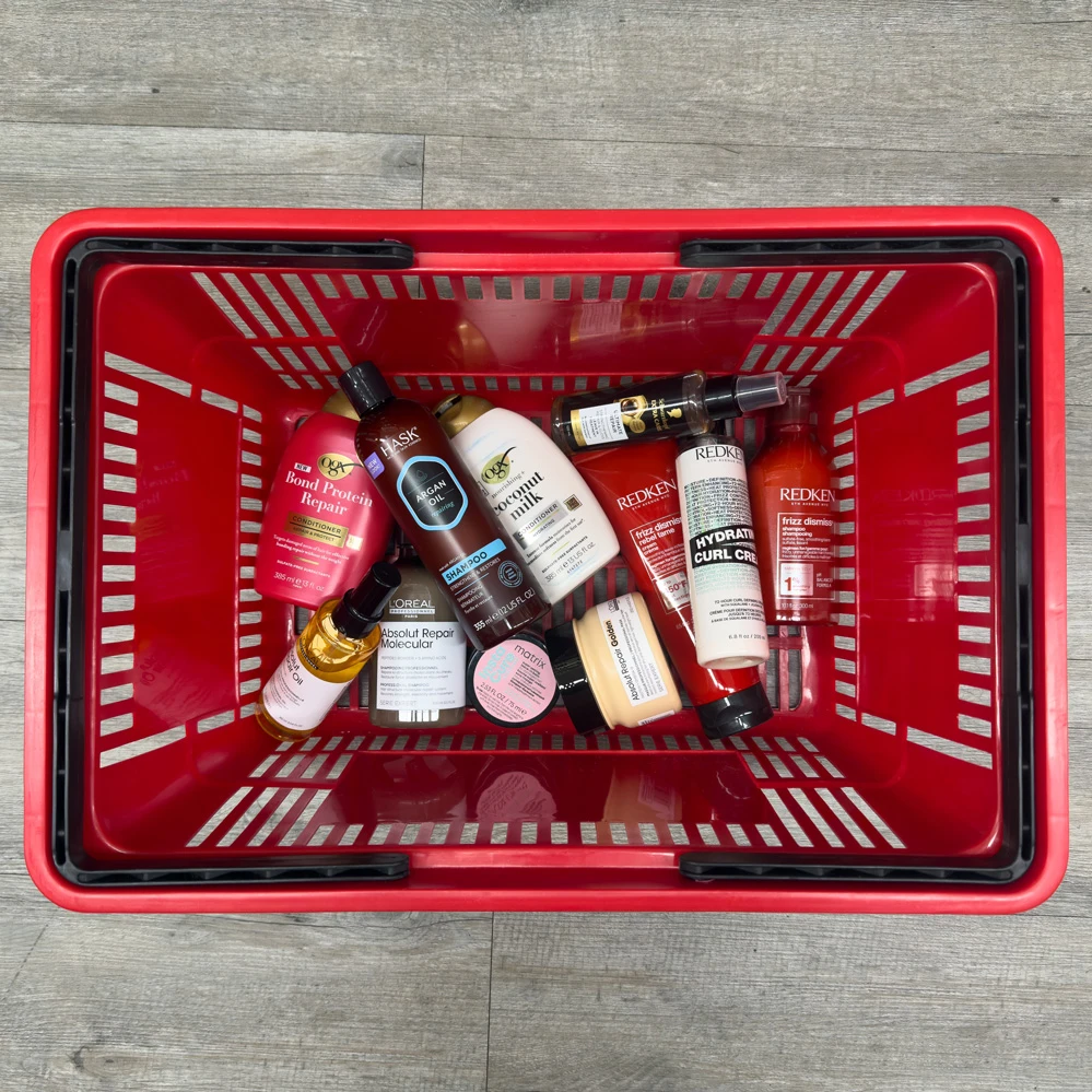 Red shopping basket filled with various hair care products including shampoos, conditioners, and treatments from brands like Redken and L'Oreal.