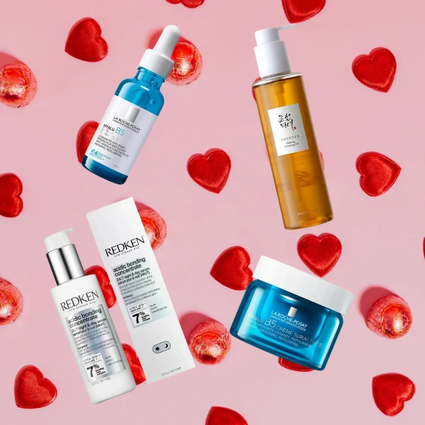 Beauty and skincare products arranged on pink background with scattered red heart decorations