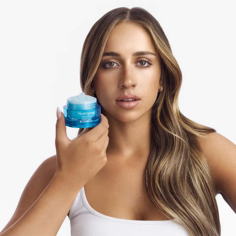 Tate McRae in white top holds blue Neutrogena skincare jar against white background.