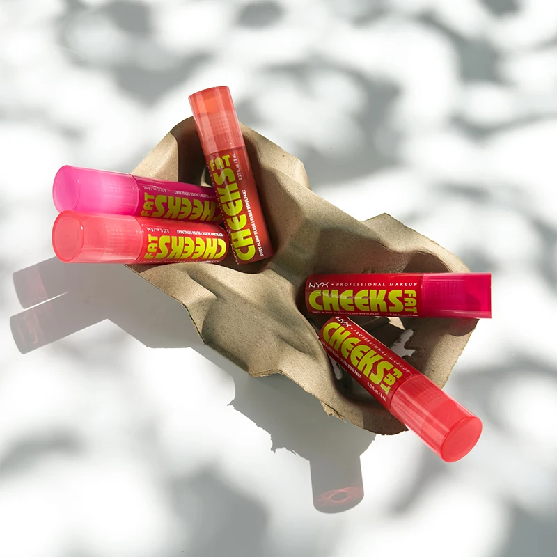 Several pink and red NYX Cheeks lip products scattered on crumpled brown paper against a light background. 