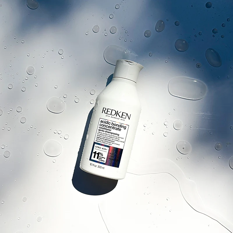 White Redken Acidic Bonding Concentrate bottle against misty background with water droplets.