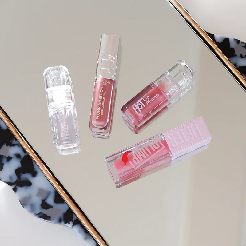 Four pink lip gloss tubes arranged on reflective surface with marble pattern visible in corner.