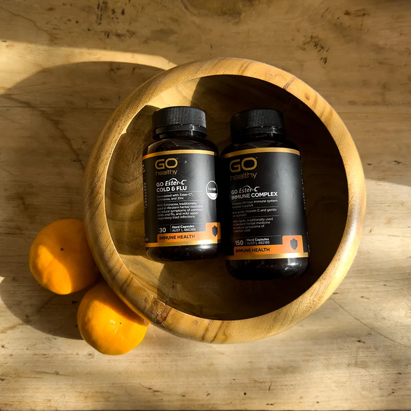 Two black GO Healthy vitamin bottles in wooden bowl with oranges, showing immune support supplements on rustic wooden surface.