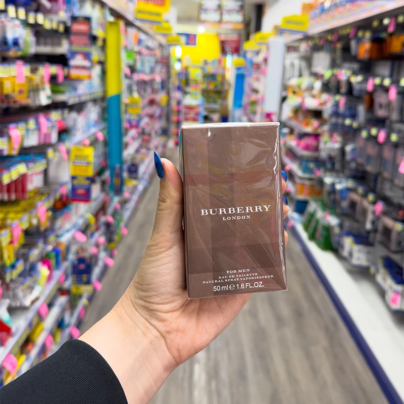 Hand holding Burberry London perfume bottle in retail store with product displays in background.