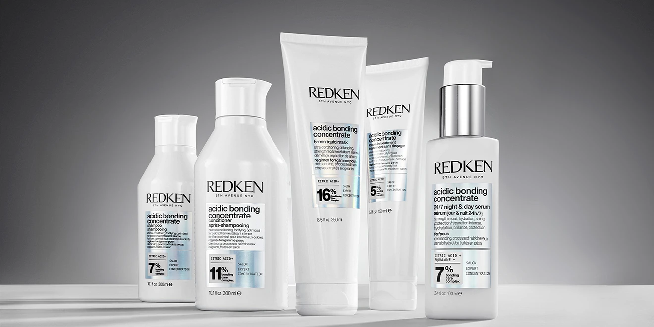 Five white Redken Acidic Bonding Concentrate hair products lined up against a gray background, showing shampoo, conditioner and treatments.