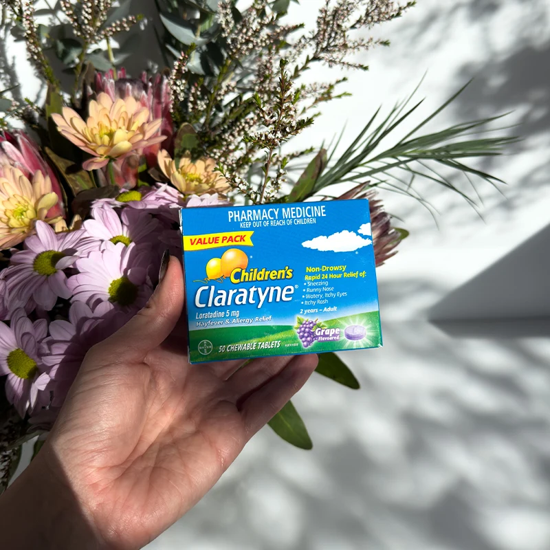 Hand holding Children's Claratyne allergy medicine box against spring flowers and foliage background