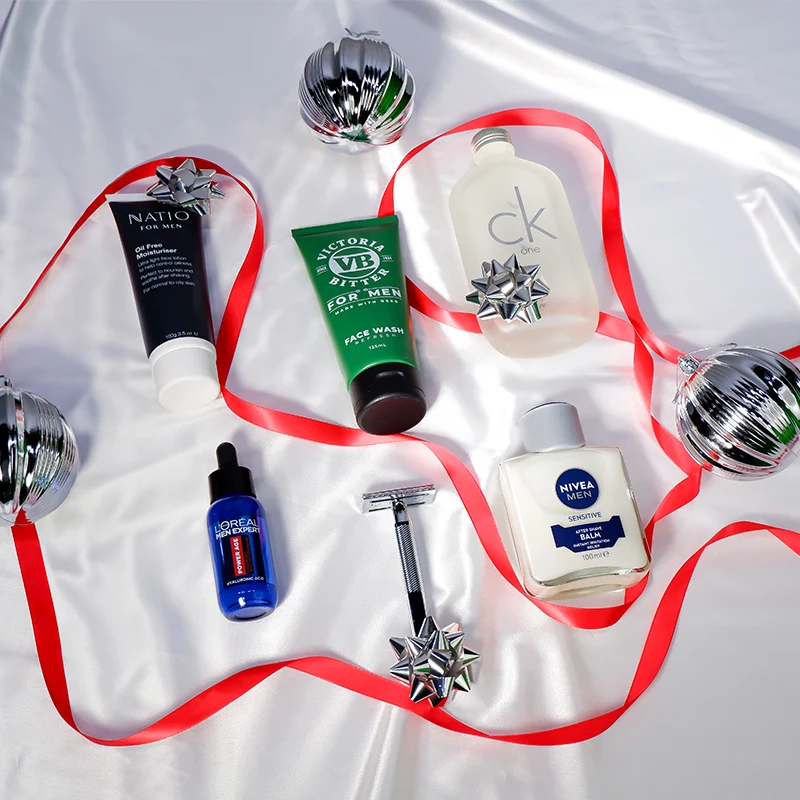 Men's grooming products and fragrances arranged with red ribbon and silver ornaments on white background.