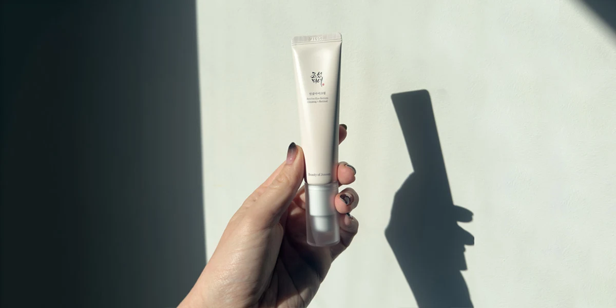 A hand holds a white tube of Beauty of Joseon Revive Eye Serum against a light wall with a soft shadow.