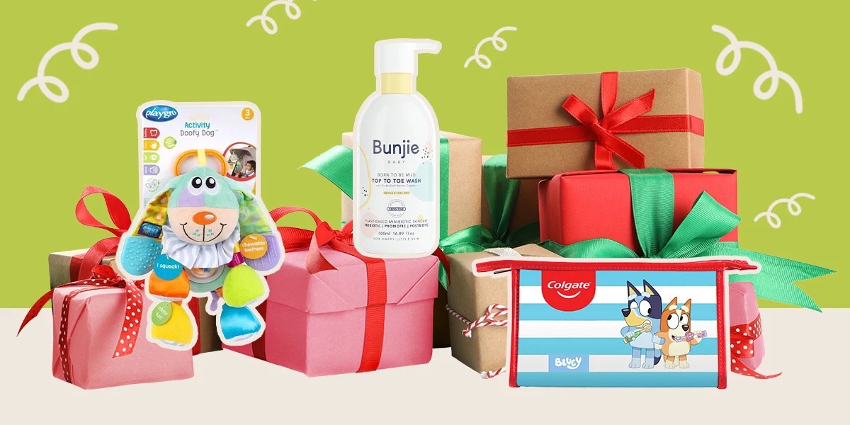 Holiday gift boxes with red and green ribbons alongside baby care products including Bunjie wash, Playtex toys, and Bluey-themed items