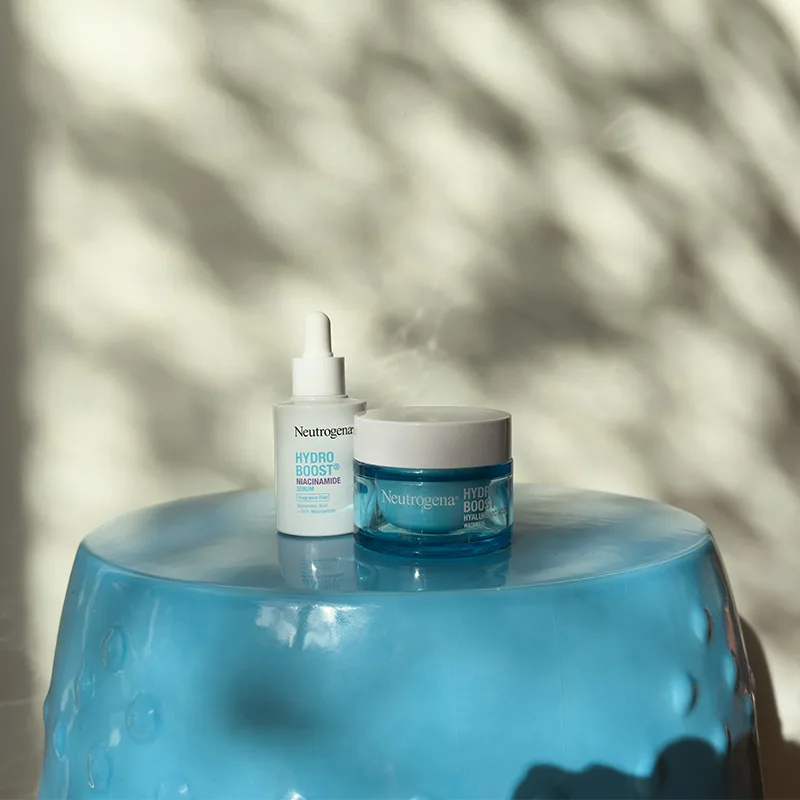 Neutrogena Hydro Boost skincare products displayed on blue glass surface with soft shadow patterns in background.