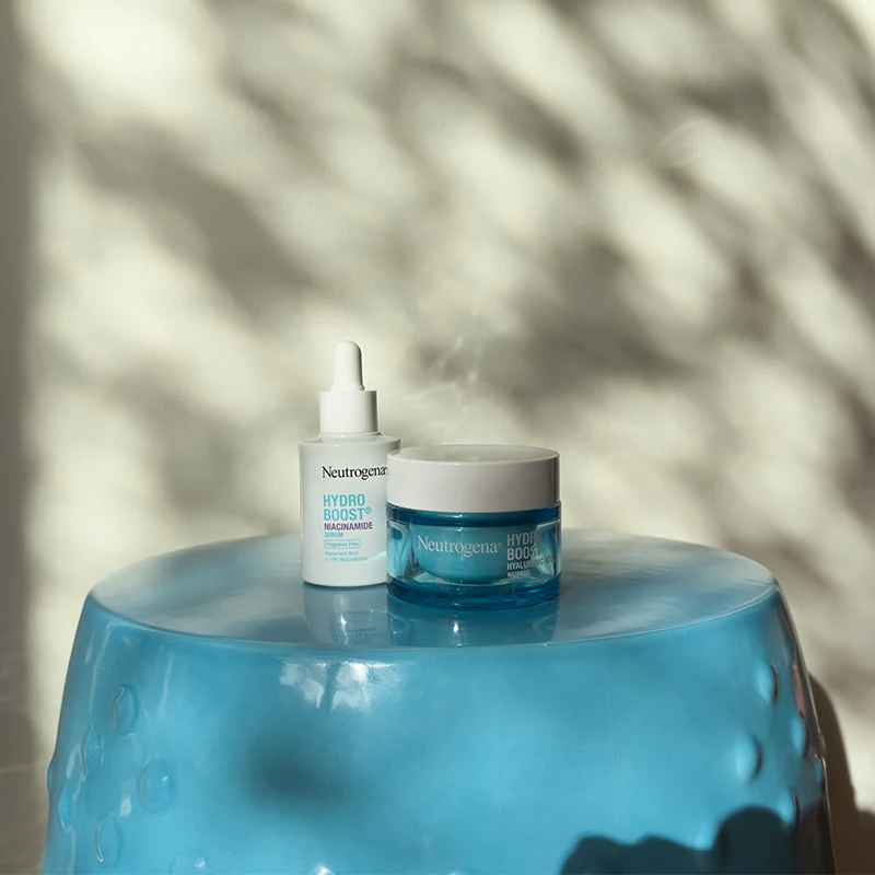 Neutrogena Hydro Boost skincare products displayed on blue glass surface with soft shadow patterns in background.