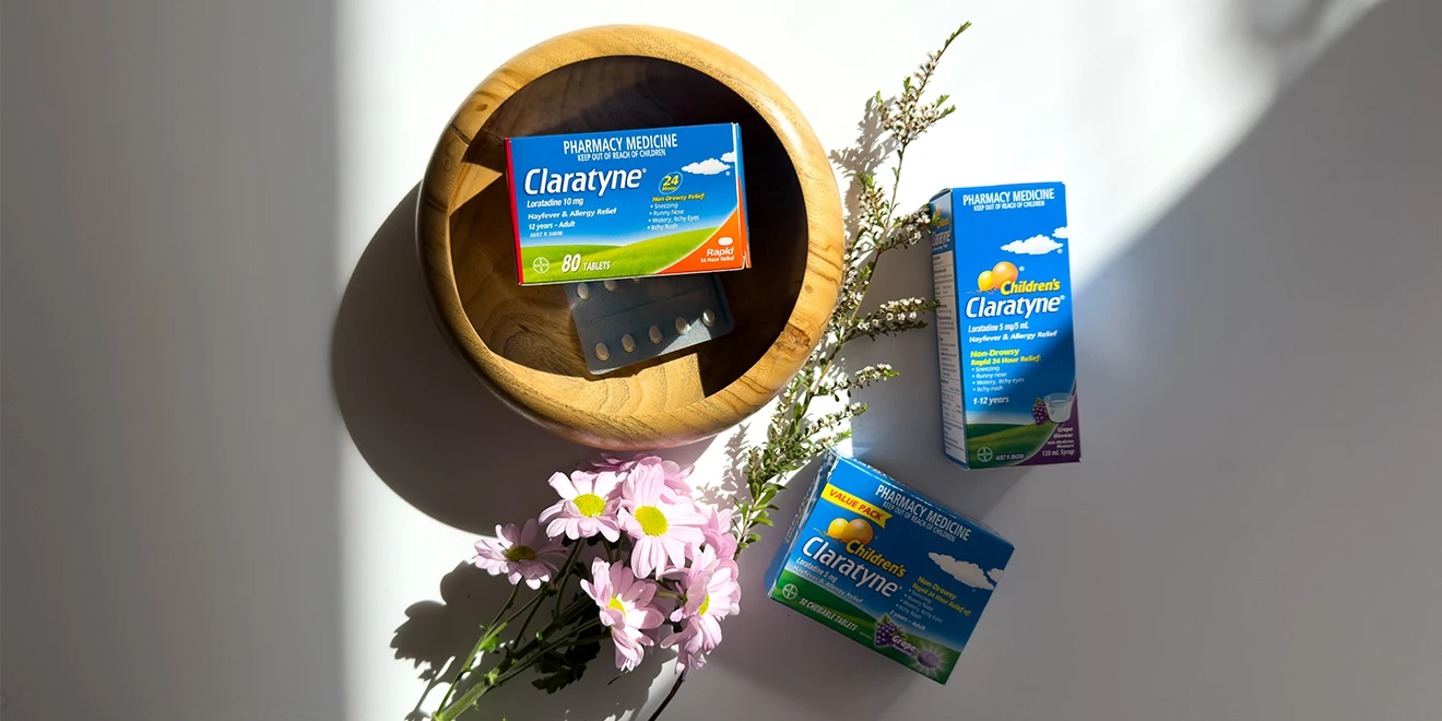 Claratyne allergy medication boxes arranged with pink daisies and a wooden bowl, casting dramatic shadows in natural light