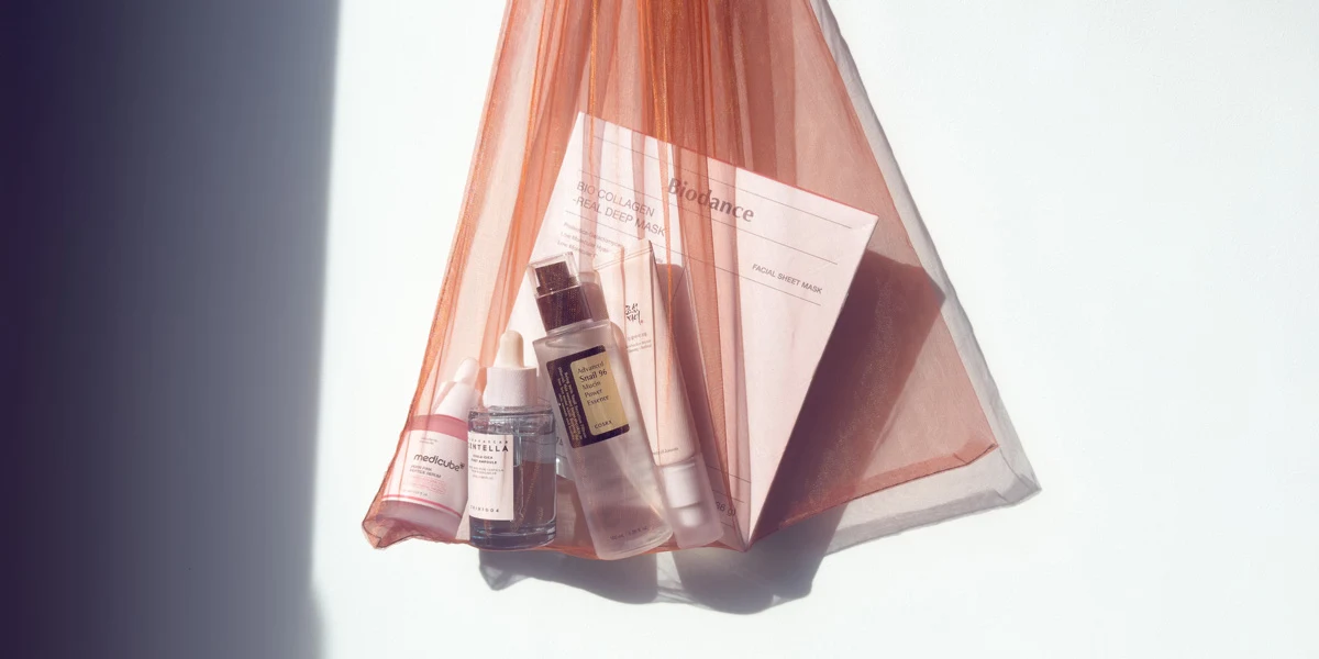 K-beauty skincare products including serums, essence, and Biodance facial sheet masks arranged in a sheer pink mesh bag on white surface.