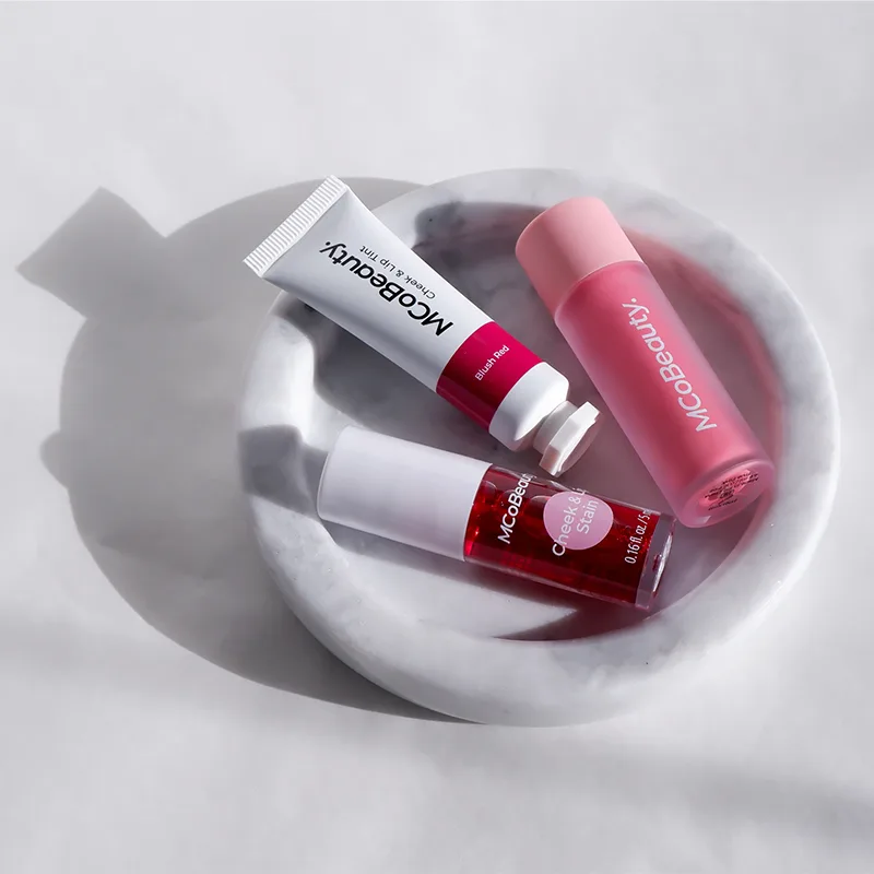 Three pink and red MCoBeauty cosmetic products arranged in a white ceramic bowl casting soft shadows.