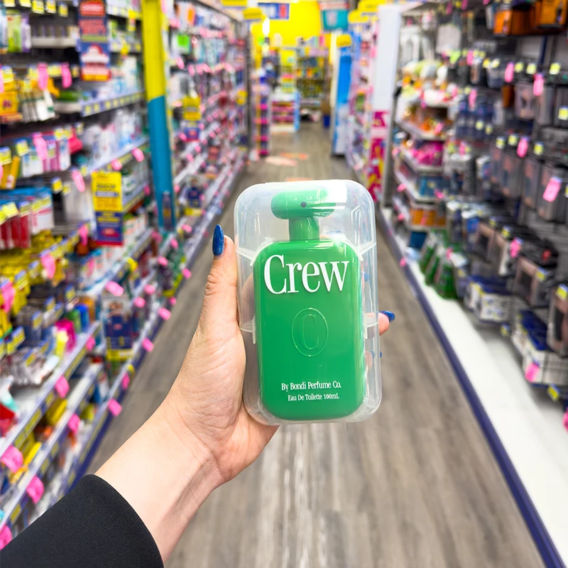 Hand holding brown IVE Guy Sebastian perfume box in retail store aisle with colorful product displays in background