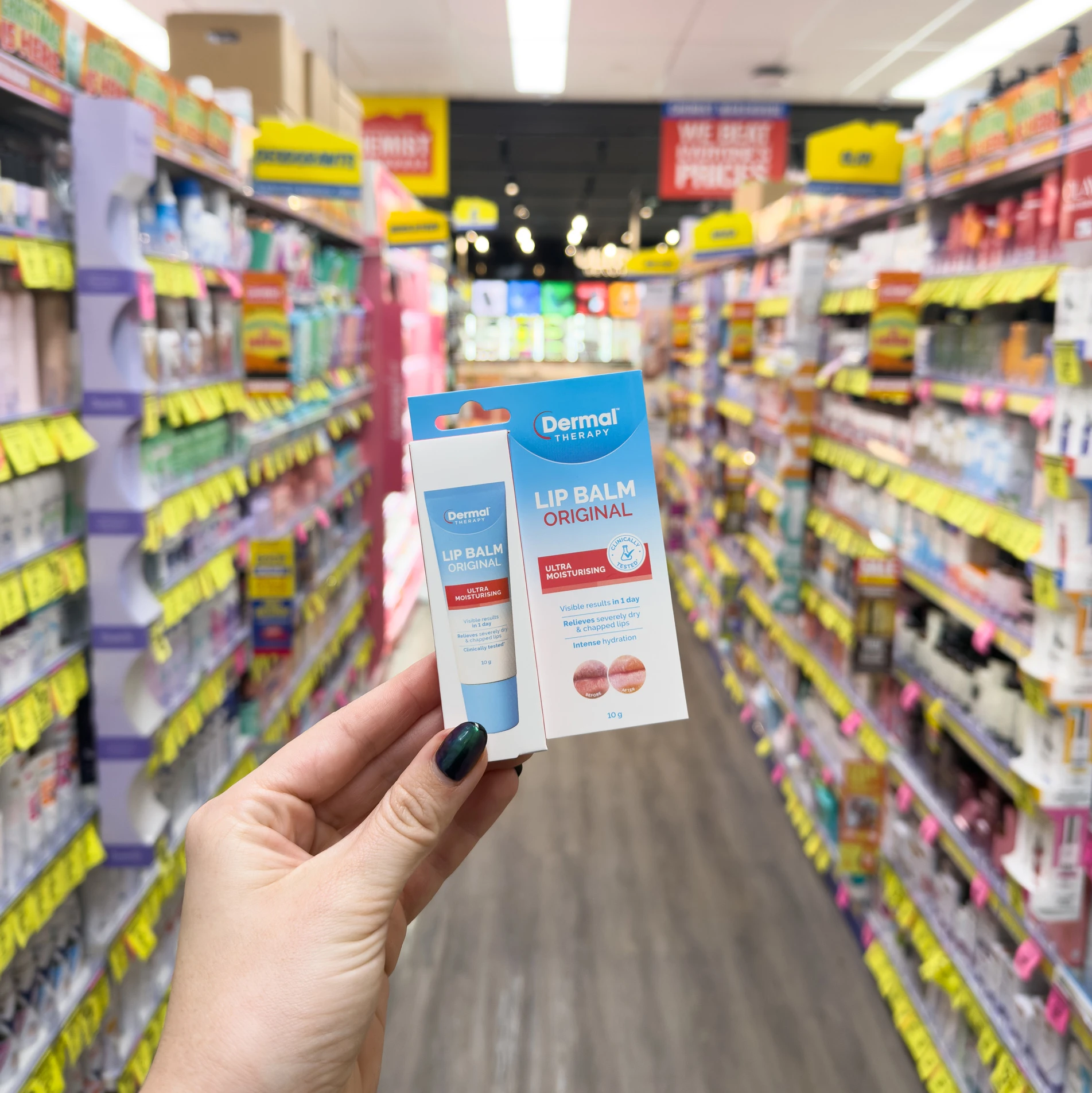 Hand holding Dermal Therapy lip balm products in Chemist warehouse aisle with colorful retail shelving and price tags in background