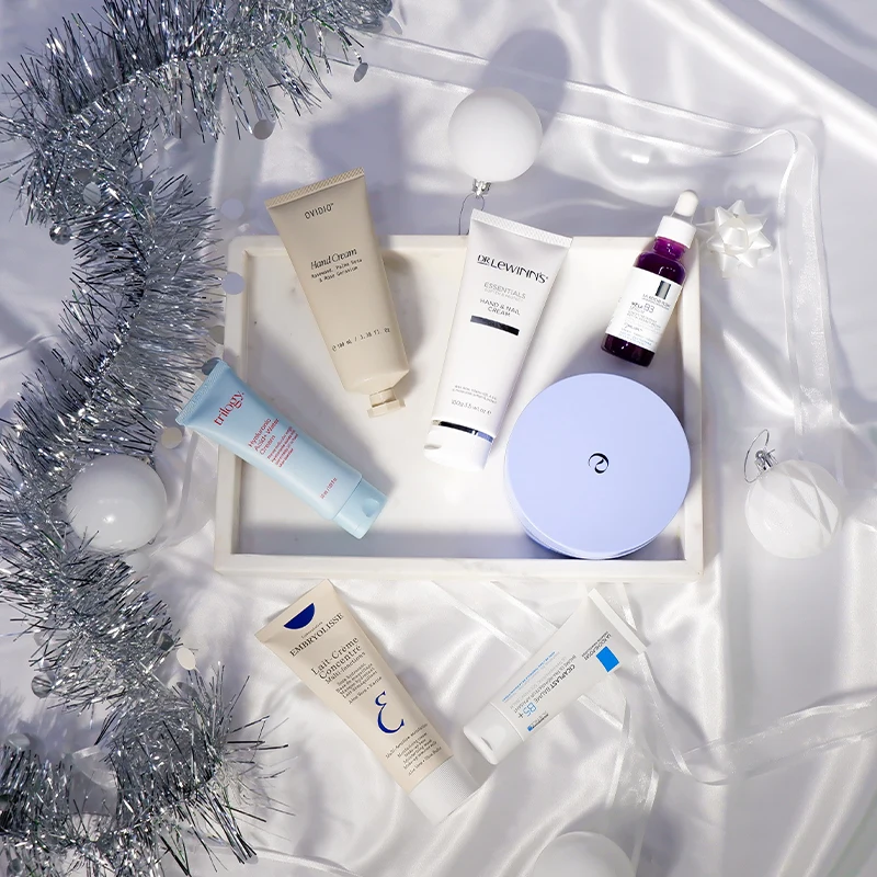 Beauty and skincare products arranged on white fabric with silver tinsel garland and ornaments creating a festive holiday display.