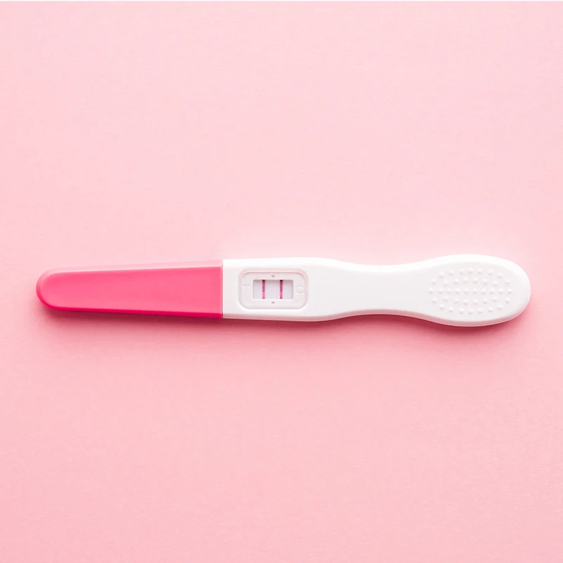 Positive pregnancy test showing two pink lines on white and pink plastic stick against pink background.