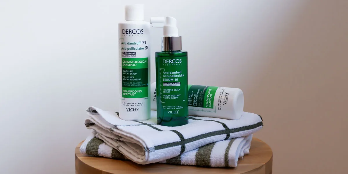 Vichy Dercos anti-dandruff hair care products in green and white bottles displayed with folded striped towels on wooden surface