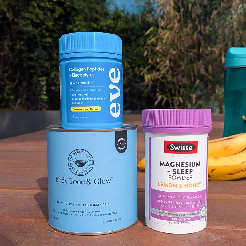 Three supplement containers outdoors: Eve Collagen Peptides, The Beauty Chef Body Tone & Glow, and Swisse Magnesium + Sleep Powder, with bananas nearby.