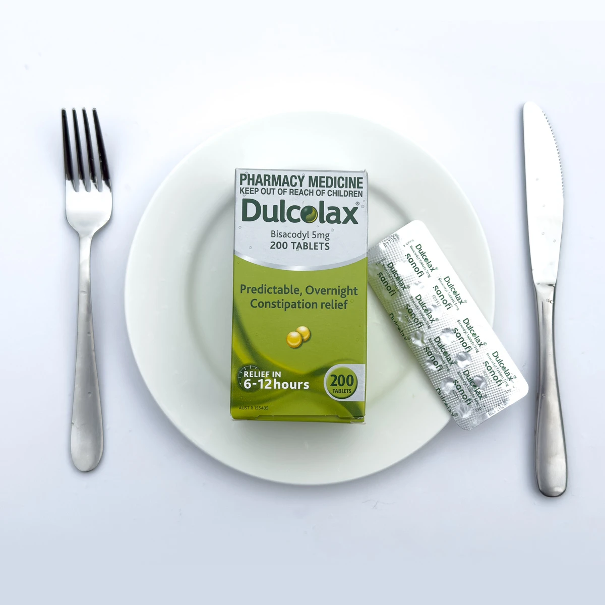 Dulcolax 200 tablet box and blister pack on a white plate, flanked by a fork and knife on a white surface.