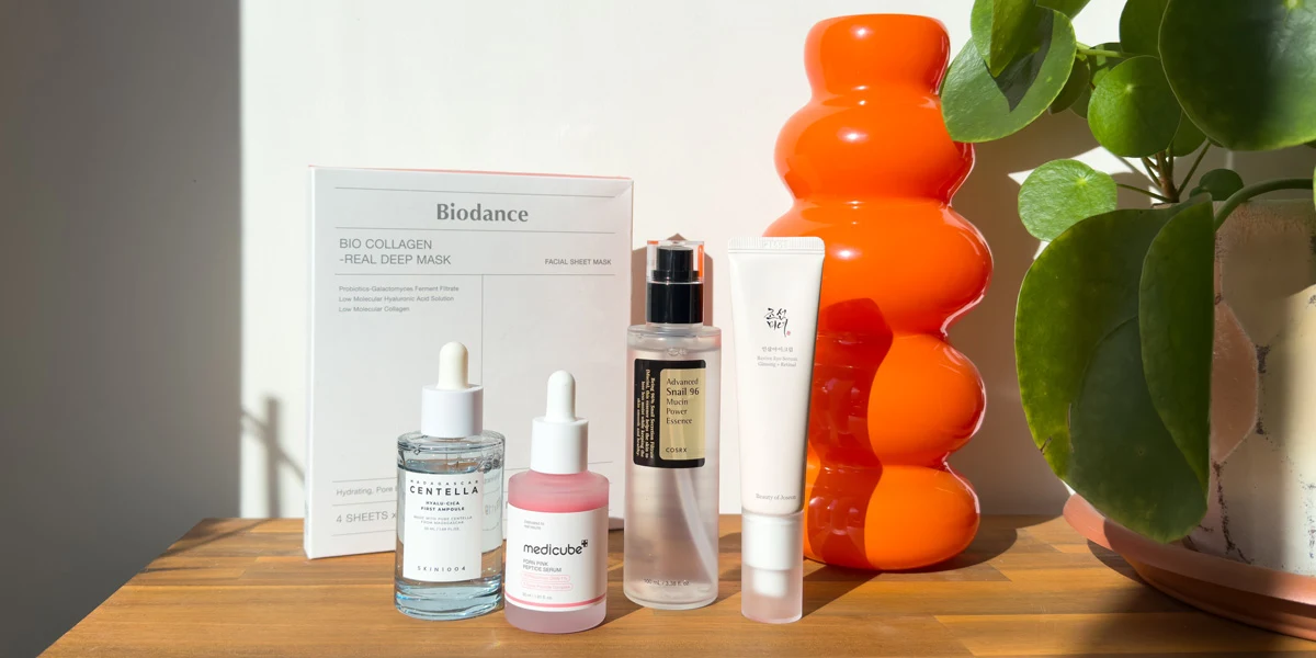 K-beauty skincare products on a wooden surface, including serums, an essence, a cream, and a Biodance collagen sheet mask box.