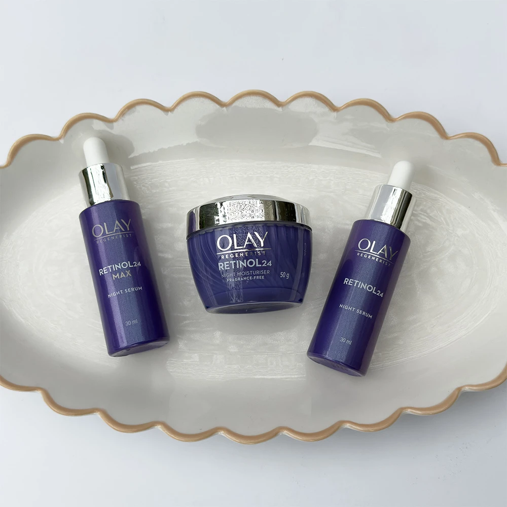 Three purple Olay Retinol24 skincare products displayed on a white scalloped plate - two serums and one night moisturizer
