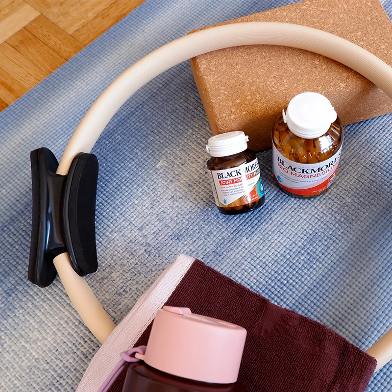 Exercise equipment including a resistance band, workout towel, and Blackmores supplement bottles on a blue yoga mat.