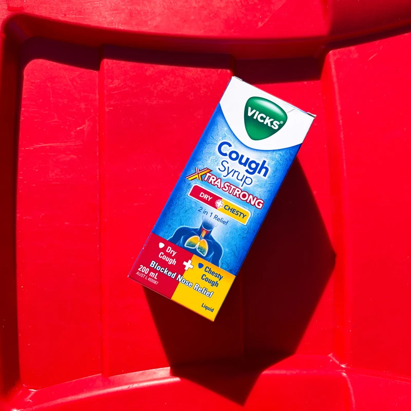 Vicks Cough Syrup Xtra Strong box for dry and chesty coughs, 200ml, placed on a bright red surface.