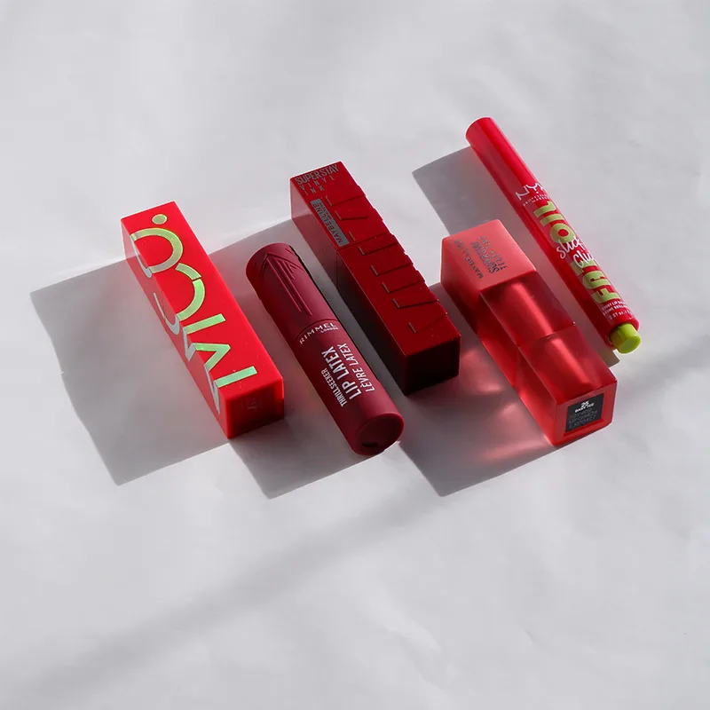 Red lipstick products and packaging arranged in a row on white background with dramatic shadows.