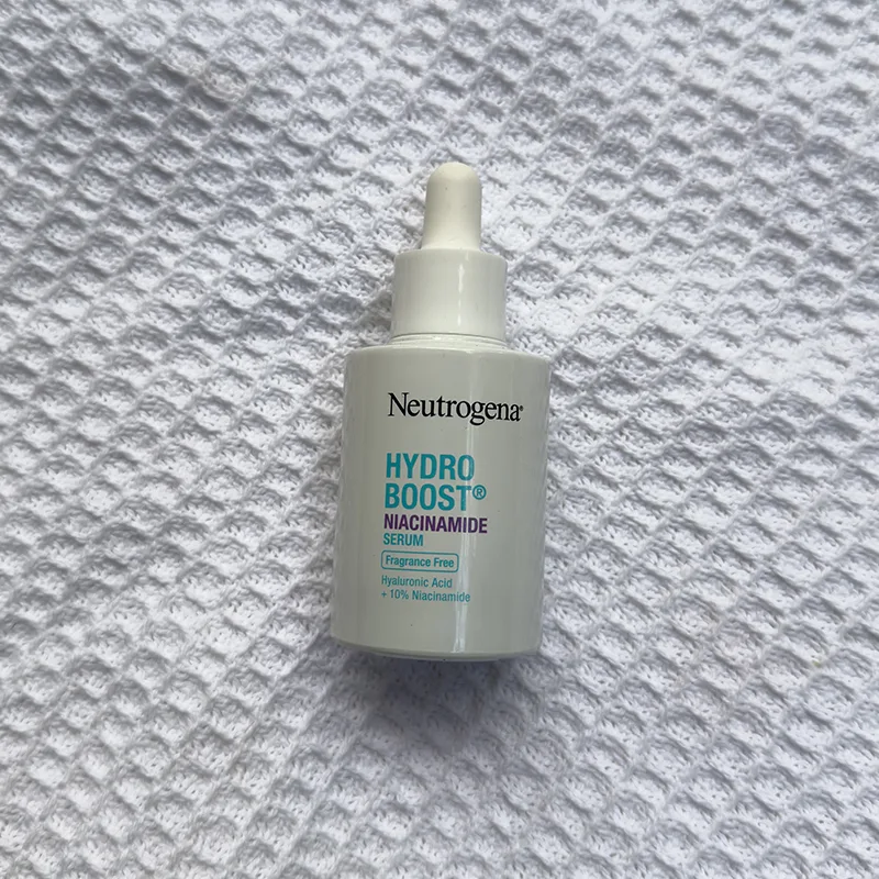 Neutrogena Hydro Boost niacinamide serum bottle with dropper on white textured fabric background.