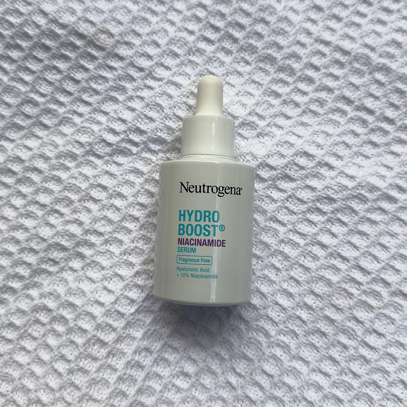 Neutrogena Hydro Boost niacinamide serum bottle with dropper on white textured fabric background.