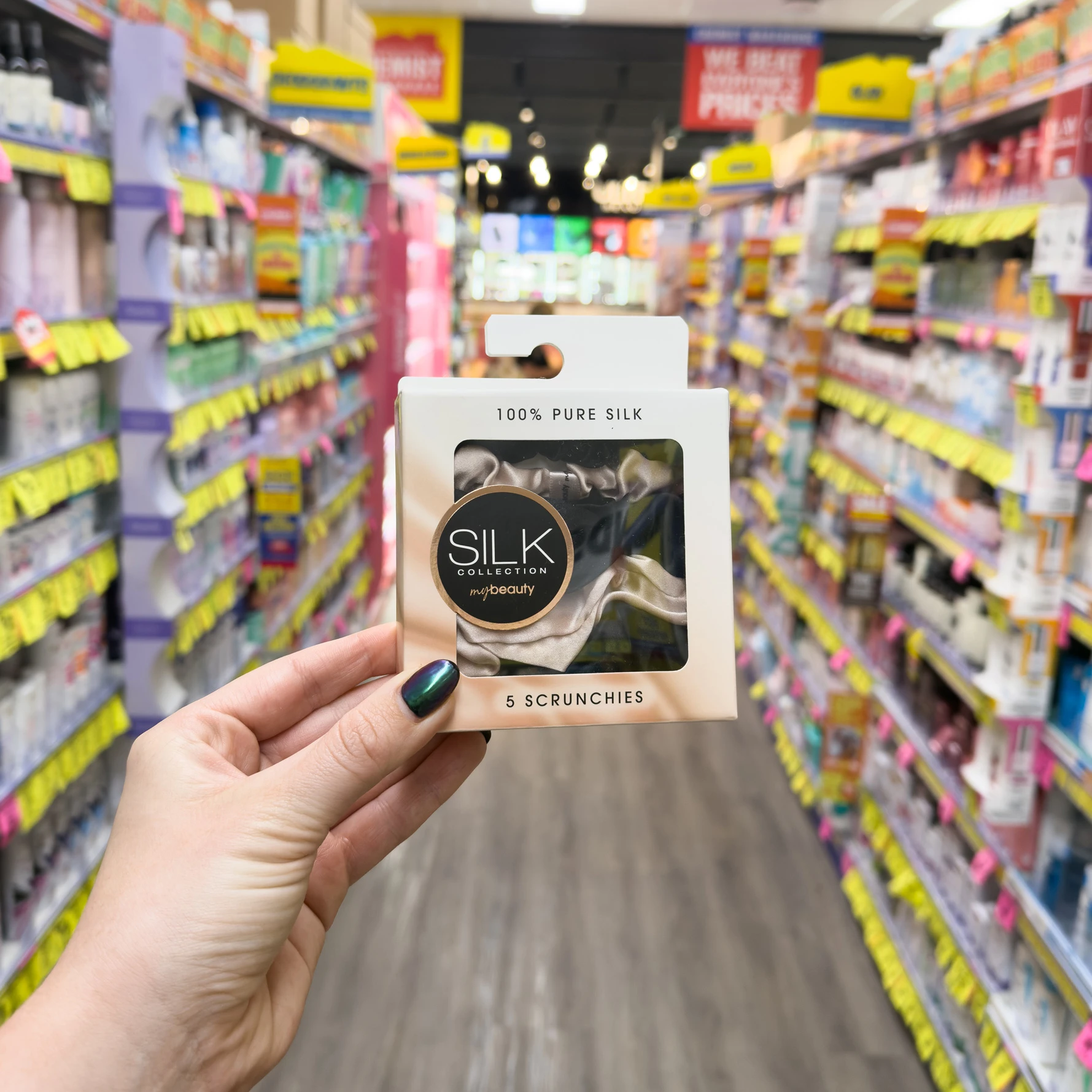 Hand holding a package of Silk Collection pure silk scrunchies in a store aisle with colorful product displays in background