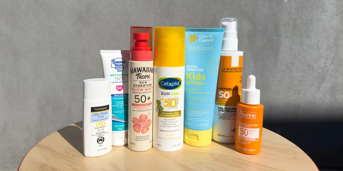 Various sunscreen products displayed on a wooden table, including brands like Neutrogena, Hawaiian Tropic, Cetaphil, Cancer Council, and Avène.