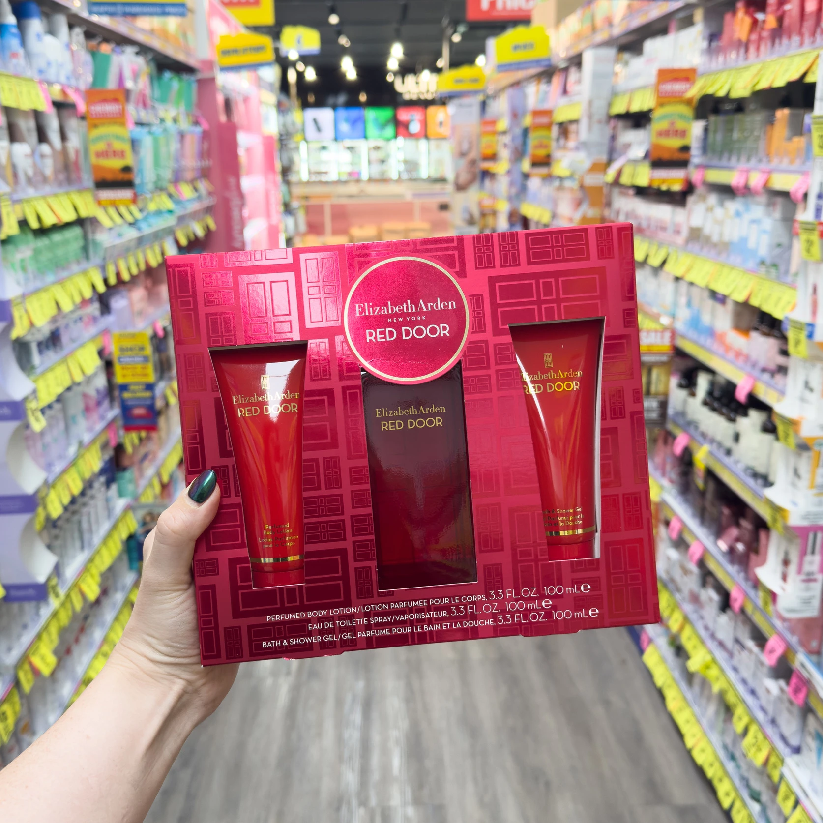 Hand holding Elizabeth Arden Red Door fragrance gift set in retail store with colorful product displays in background
