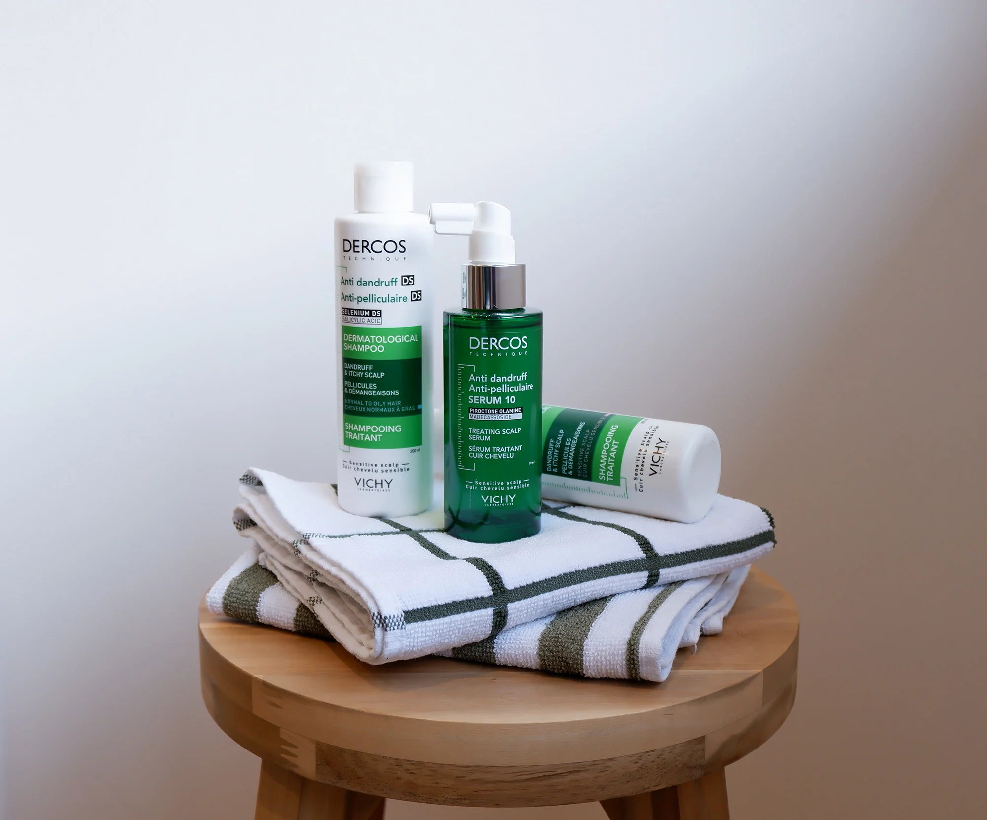 Vichy Dercos anti-dandruff hair products displayed on folded white and green striped towels atop wooden stool.