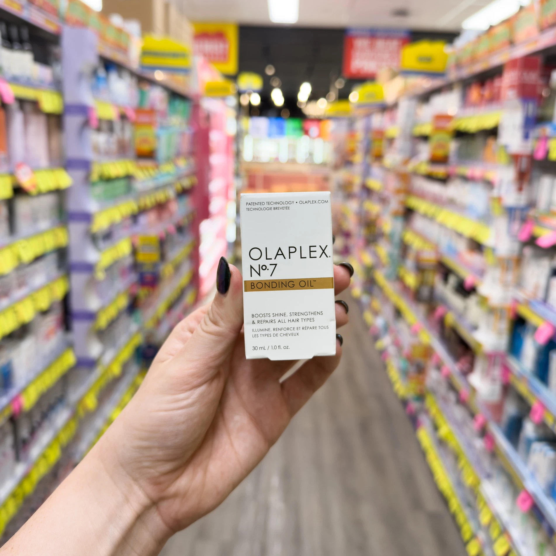 Hand holding Olaplex No.7 Bonding Oil product box in a store aisle with colorful beauty product shelves in background